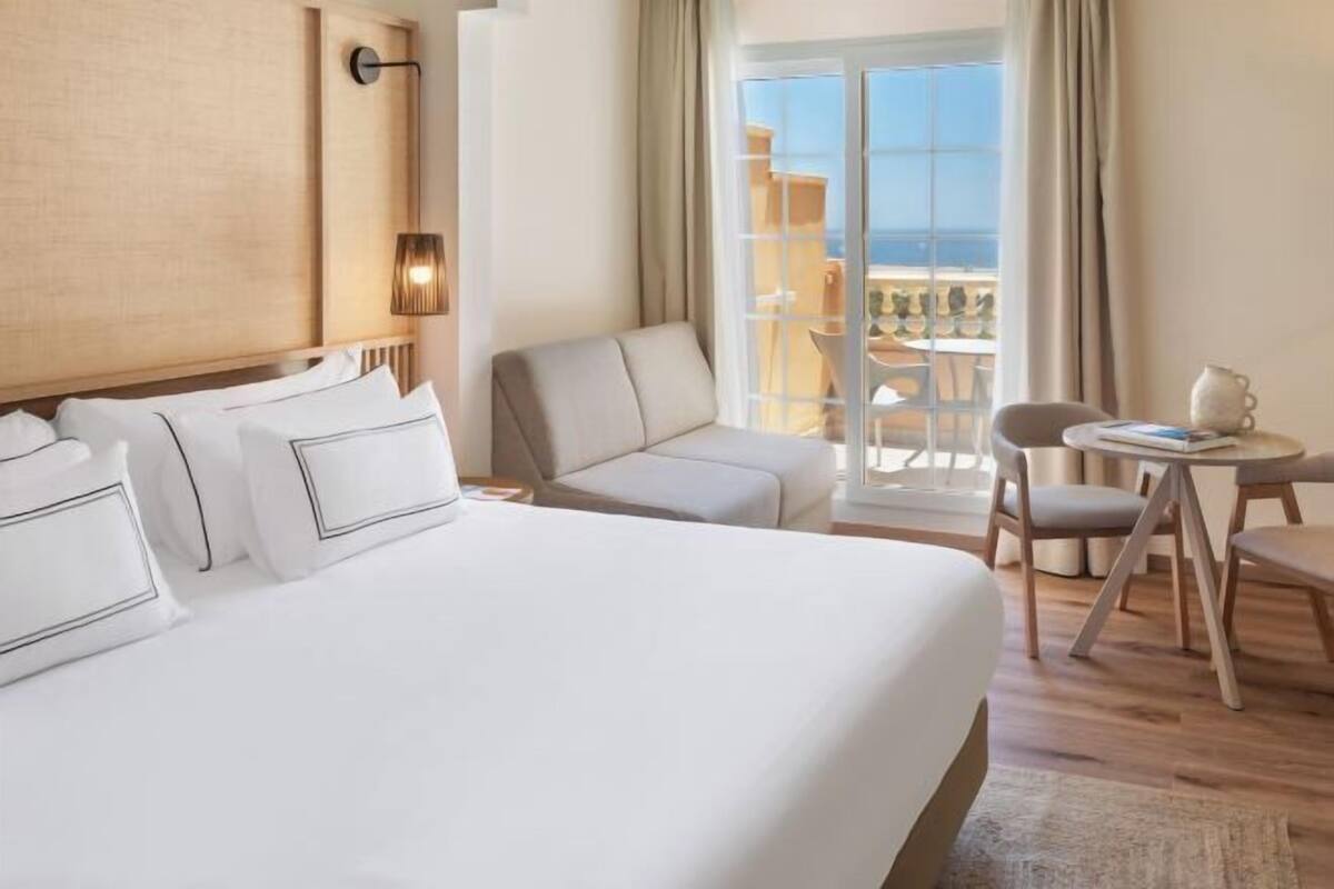 Une chambre d’hôtel avec un grand lit, un canapé, une petite table et un balcon avec vue.