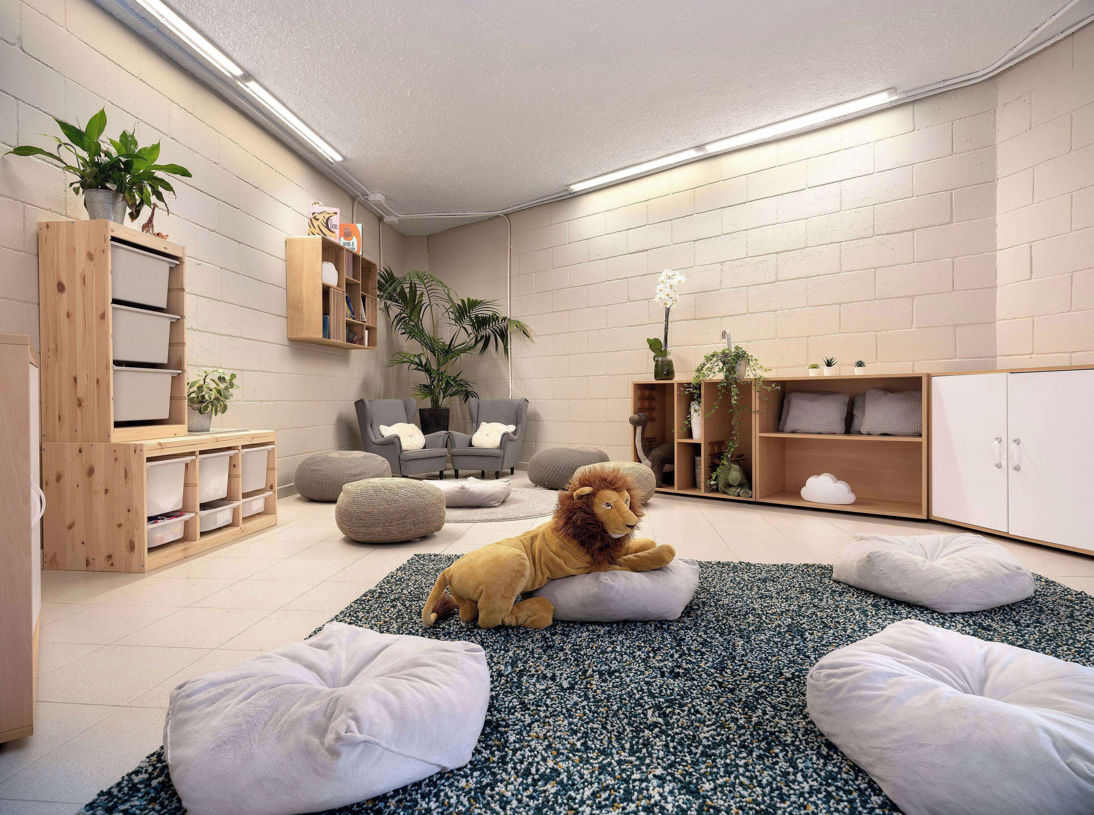 Ein gemütliches Zimmer mit einem weichen Löwenkuscheltier, Stauraumeinheiten, einem grauen Sessel und einem Bücherregal.