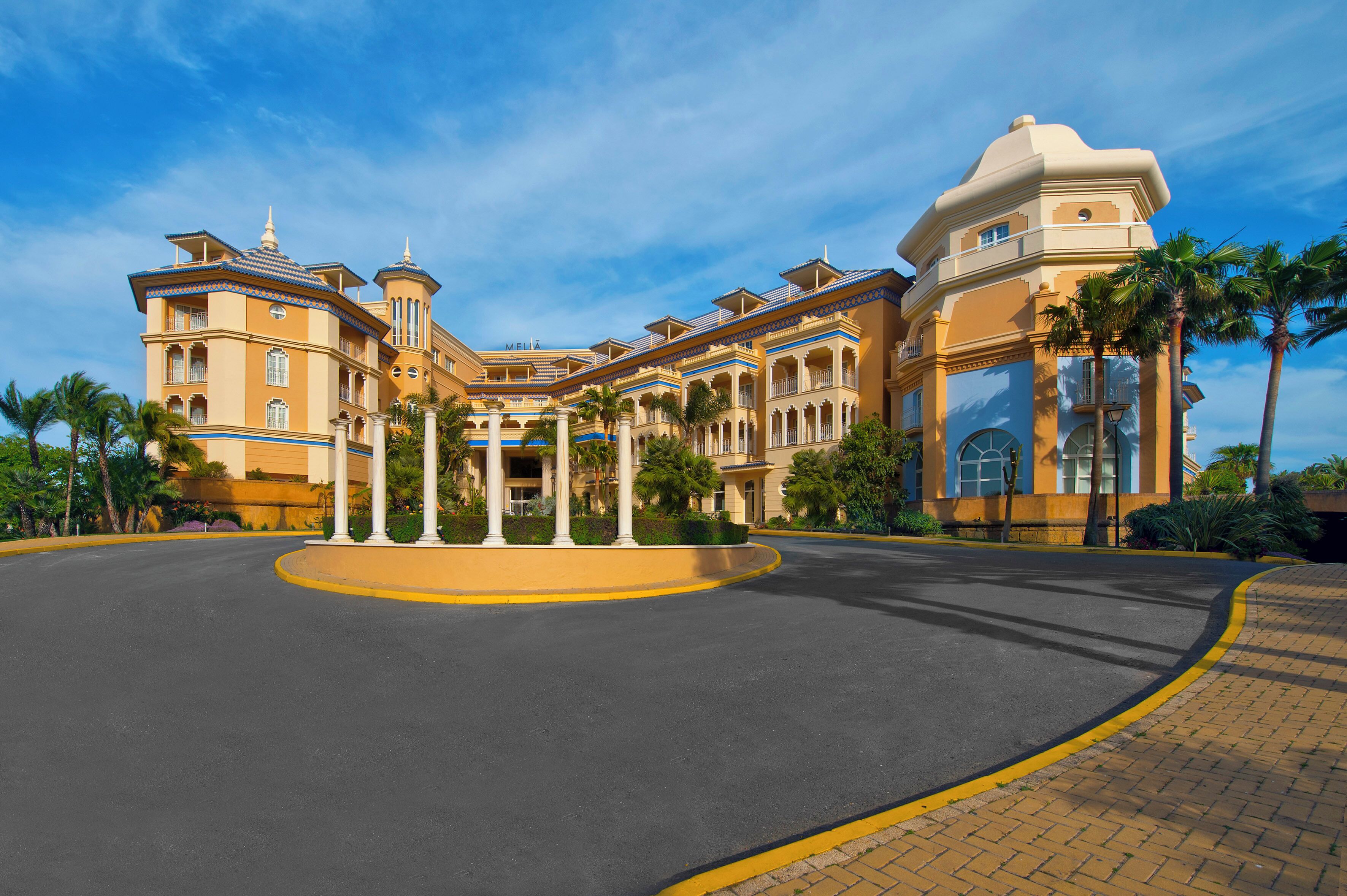 Un grand hôtel à plusieurs étages, doté d’une cour intérieure, de palmiers et surplombant un ciel d’un bleu éclatant.