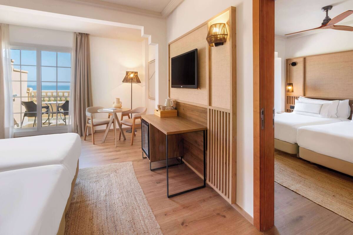 Une chambre d’hôtel avec deux lits, un bureau, une télévision et un balcon donnant sur la mer.