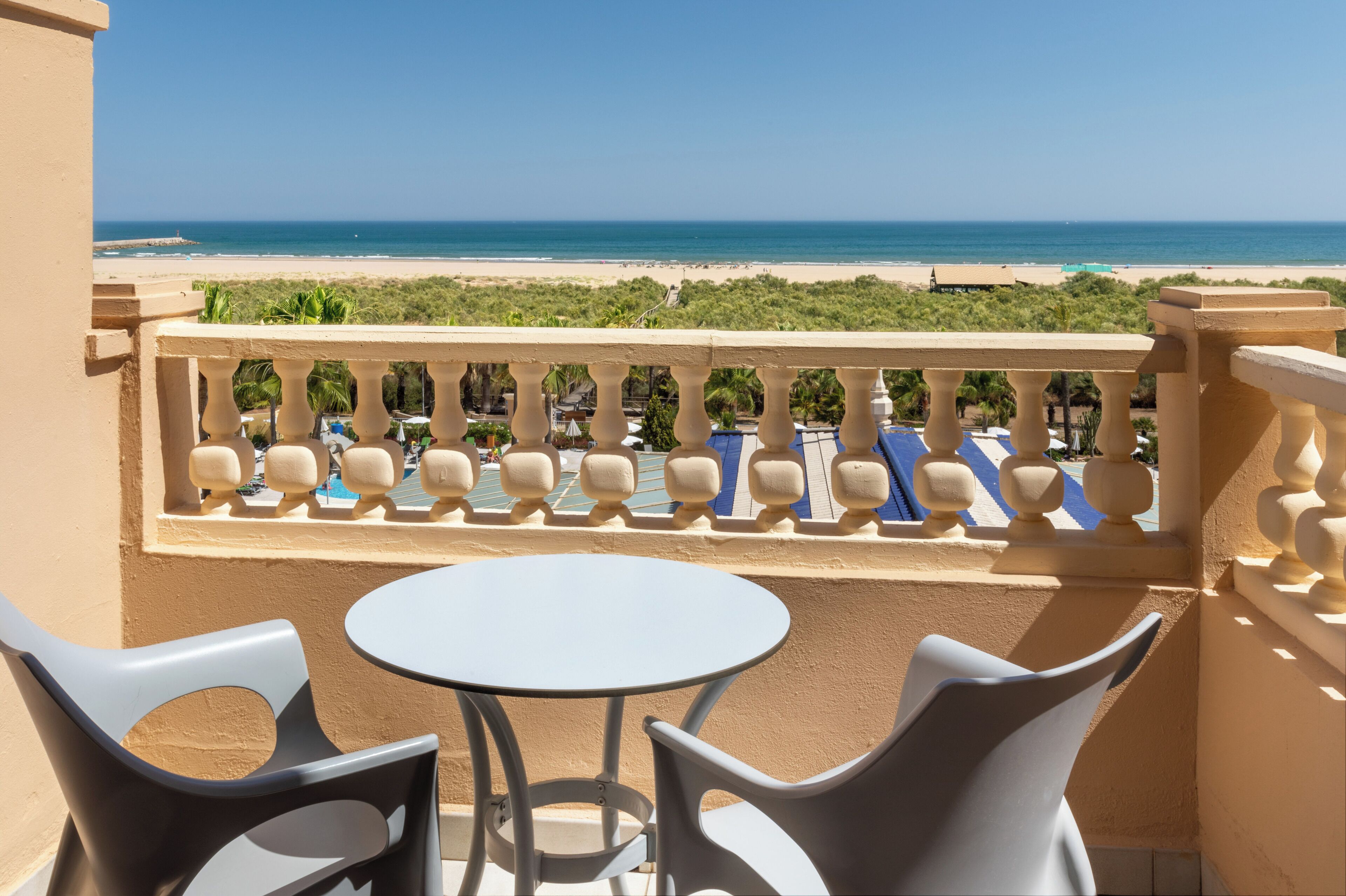 Un balcón con vista a la playa, una mesa redonda y dos sillas.