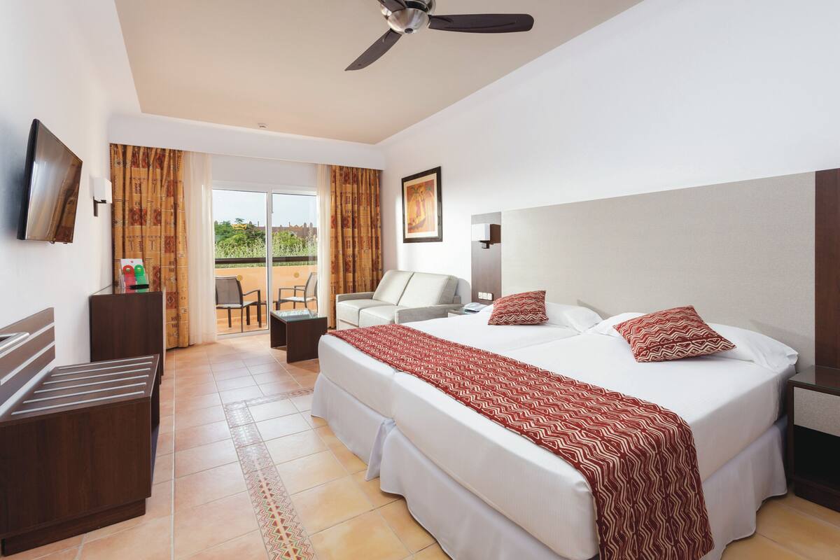 A hotel room with a bed, a desk, a chair, a TV, and a balcony with a view.