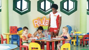 Un aula con niños realizando actividades, mobiliario colorido y un cartel educativo grande en la pared.