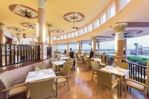 A spacious indoor dining area with high ceilings, large windows, and a view of the sea.
