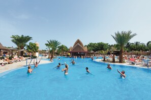 A large outdoor swimming pool surrounded by palm trees and lounge chairs, with a distinctive building in the background.