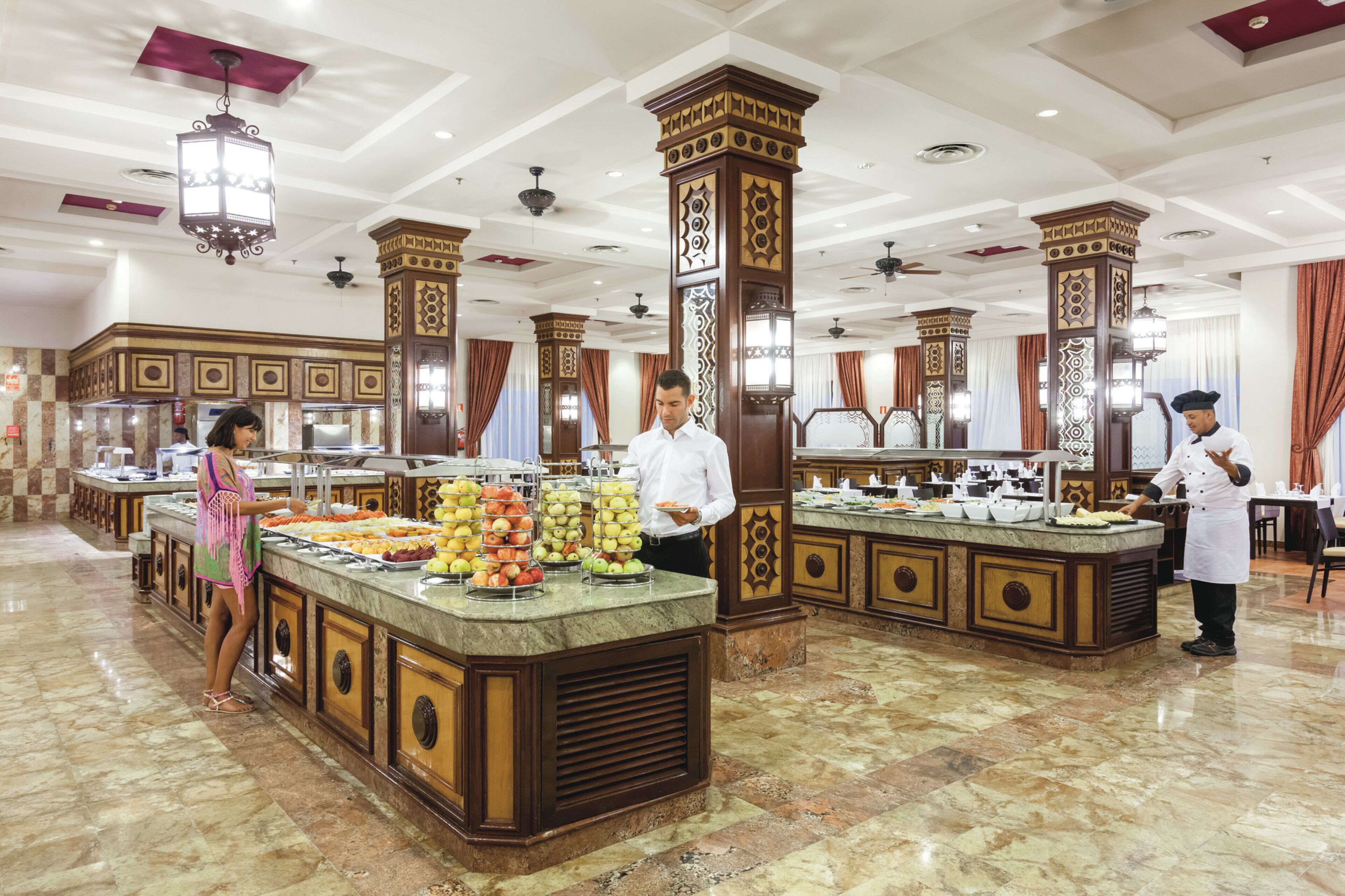 A buffet area with a marble floor, decorative pillars, and a variety of food items displayed on a central island.