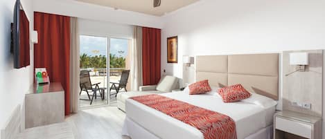 Une chambre d’hôtel comprenant un lit, un bureau, une chaise, une télévision et un balcon avec vue sur les palmiers.