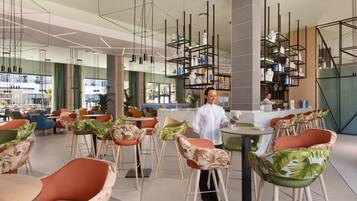 A modern restaurant with high ceilings, pendant lighting, and a variety of seating options including bar stools and chairs.