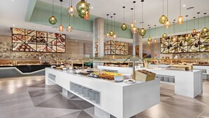 En moderne morgenmadsbuffet med flere serveringsstationer, vægge med geometrisk mønster og hængende, kugleformede pendellamper.
