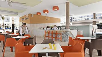 Un espace de restauration extérieur moderne, avec des chaises orange et grises, des tables blanches et un comptoir central sur lequel est affiché un panneau indiquant « Café Blanca ».