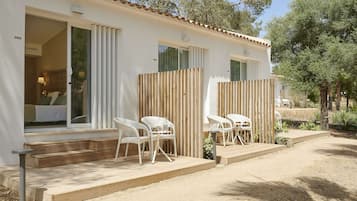 Una villa blanca con una terraza de madera, dos sillas blancas de mimbre y una pequeña mesa.