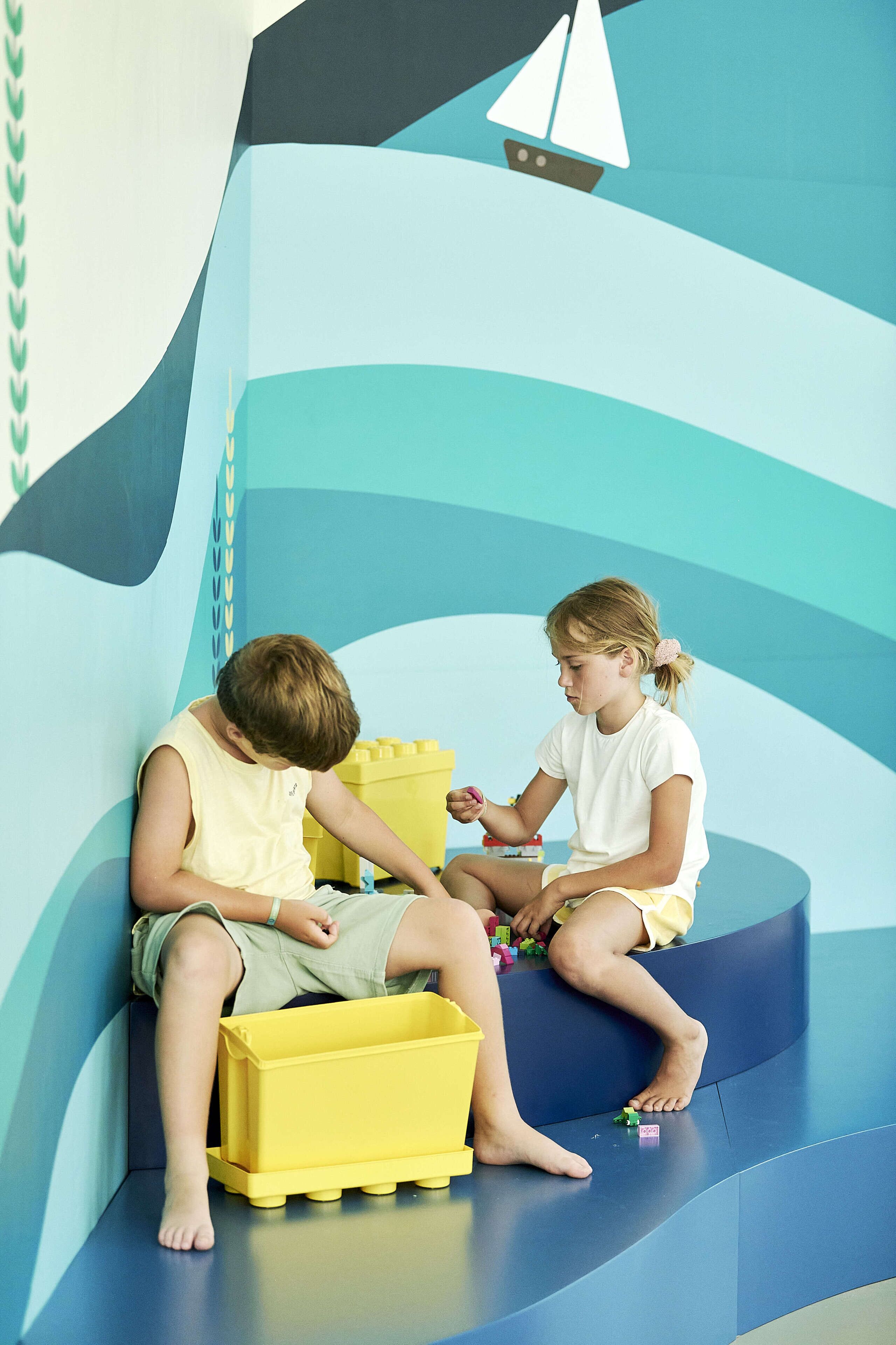 Twee kinderen spelen met speelgoed in een gebogen, blauw-witte speelruimte.