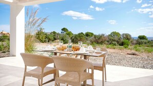 Une table à manger pour deux personnes, avec des chaises en osier, un plateau en verre et une vue sur le paysage.