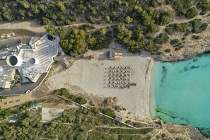 An aerial view of a coastal hotel with a beach area, a parking lot, and a small building with a sloped roof. - Iberostar Waves Cala Domingos -All Inclusive (Manacor)