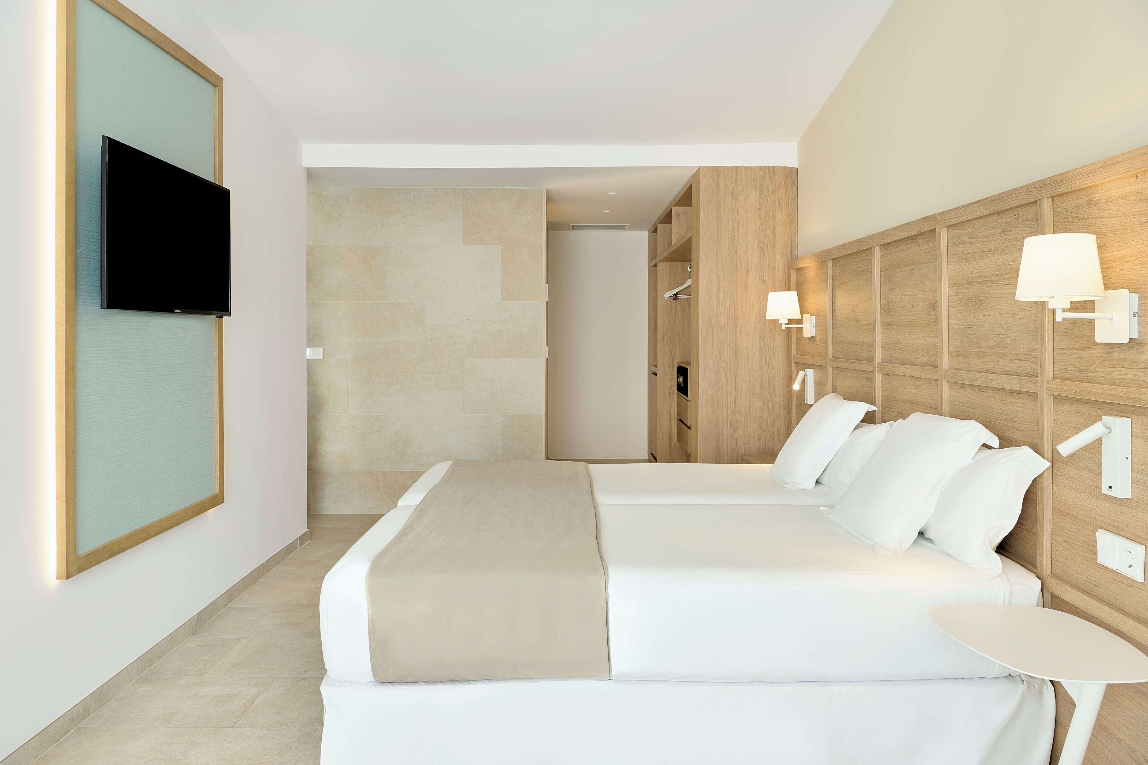 Une chambre d’hôtel moderne avec un grand lit, un téléviseur fixé au mur et une petite table.