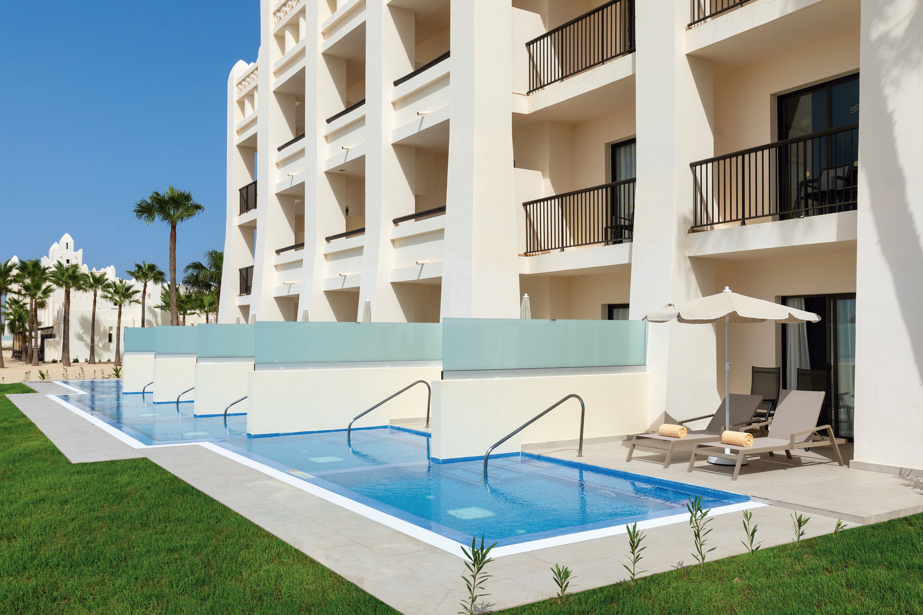 Un hotel con piscina, varios balcones y zonas de estar al aire libre.