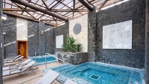 An indoor swimming pool with stone walls and tiled floor, surrounded by lounge chairs. - Hotel Riu Karamboa - Adults Only - All Inclusive (Boa Vista)