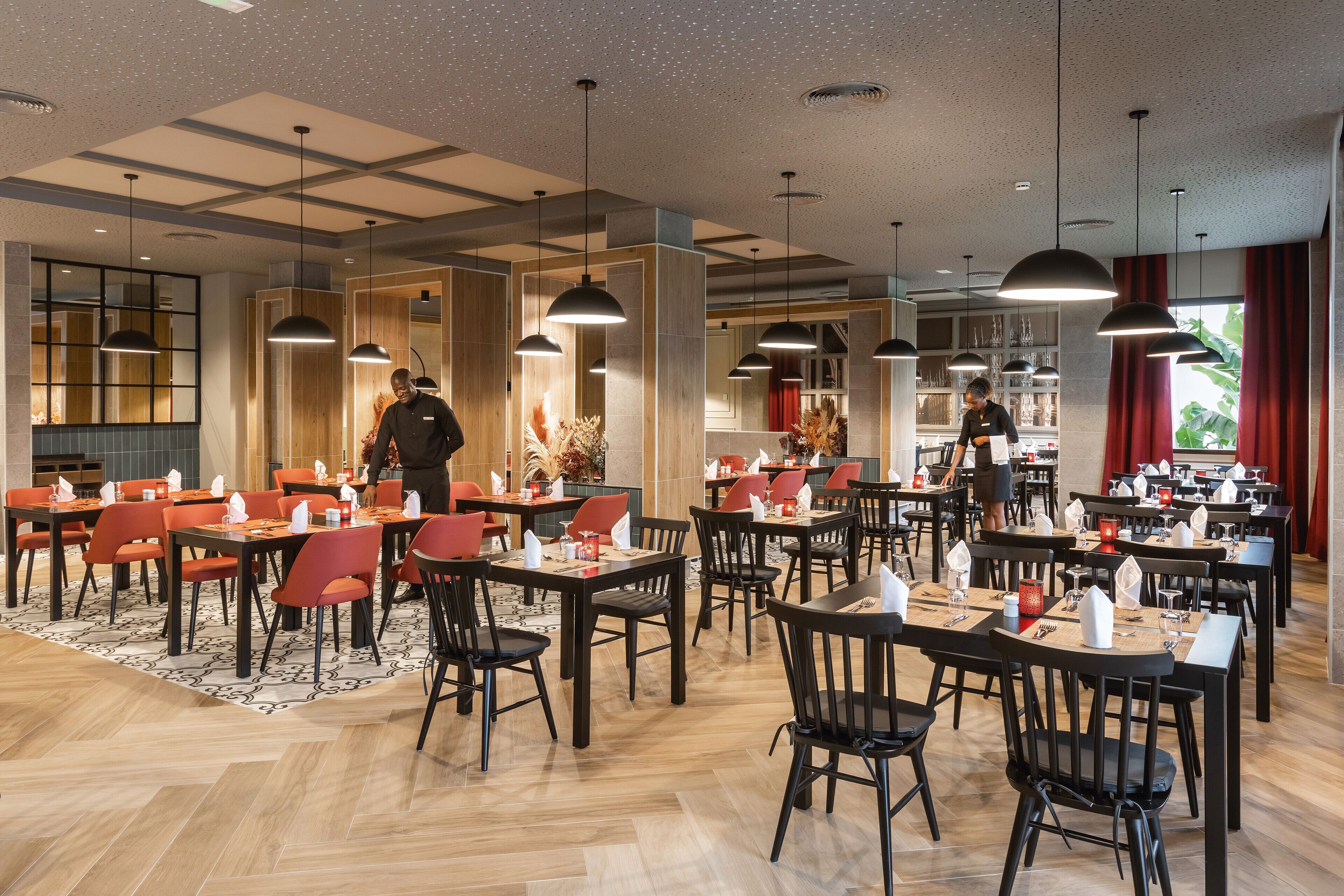 Un restaurant moderne avec un plancher en bois, des chaises noires et rouges, et des luminaires suspendus.