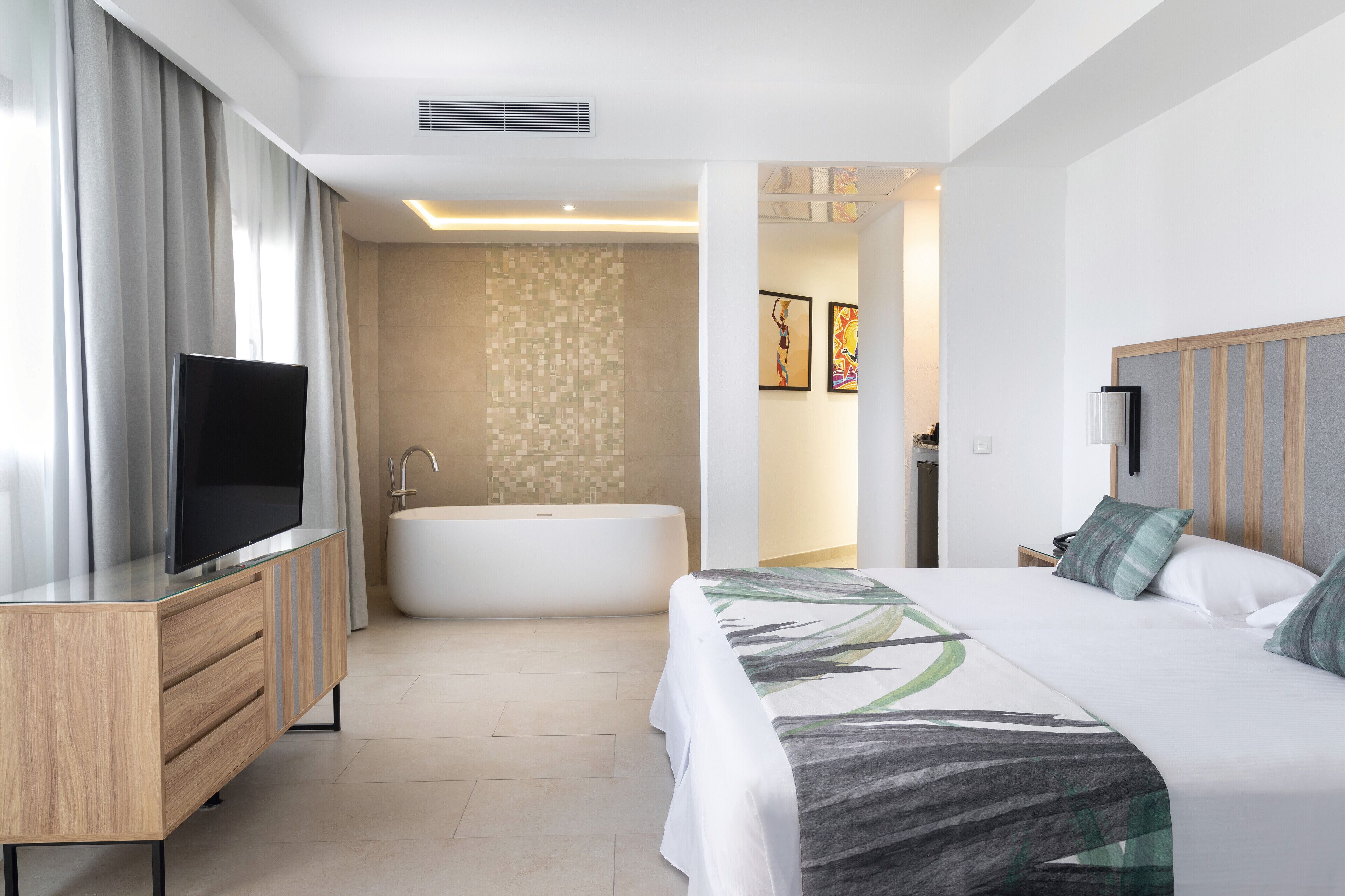 Habitación de hotel moderna con una cama grande, televisor de pantalla plana, bañera y tocador con espejo.