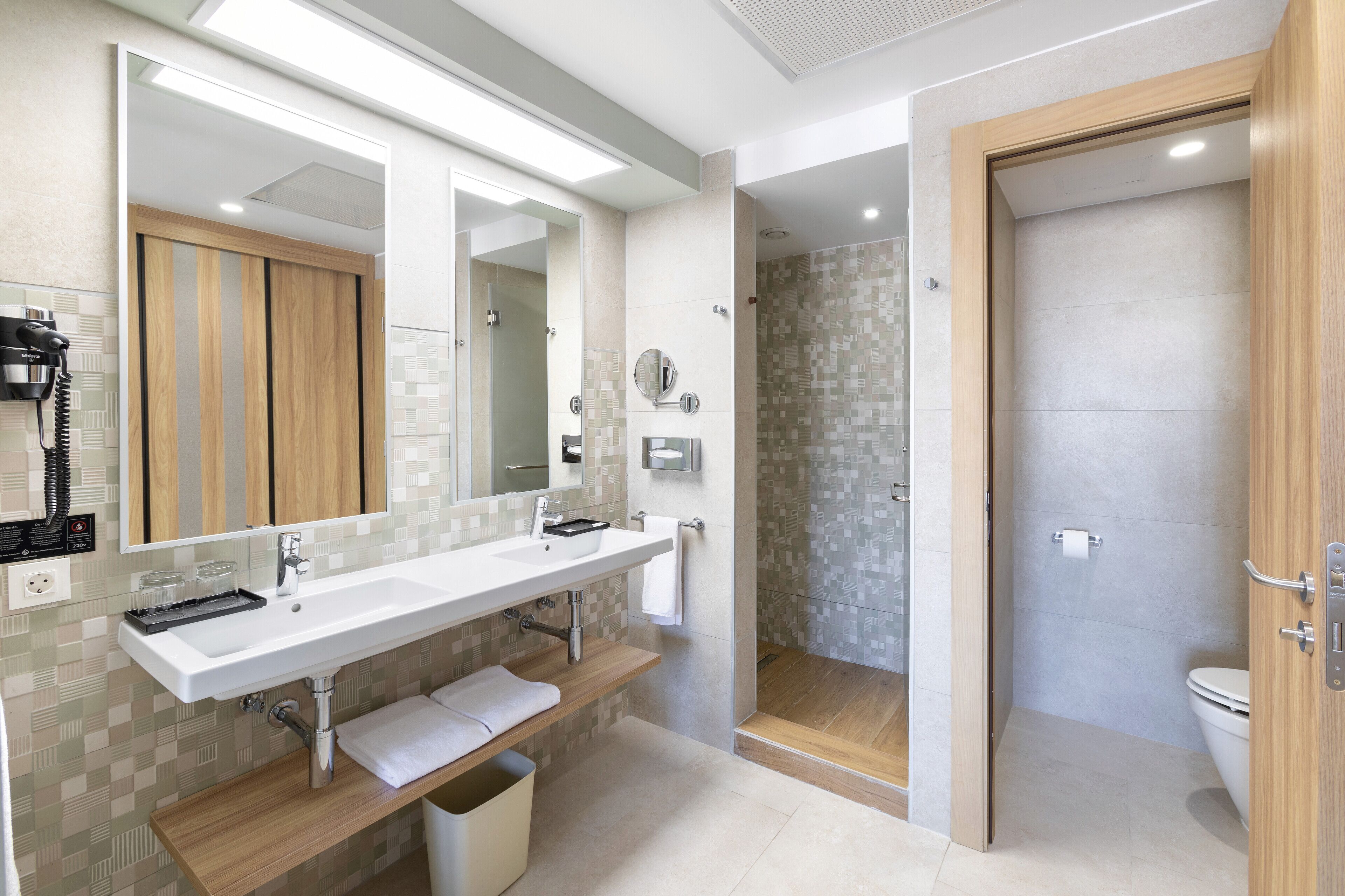 Un baño moderno con un espejo grande, dos lavamanos, una zona de ducha y un inodoro.
