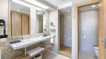 Un baño moderno con un espejo grande, dos lavamanos, una zona de ducha y un inodoro.