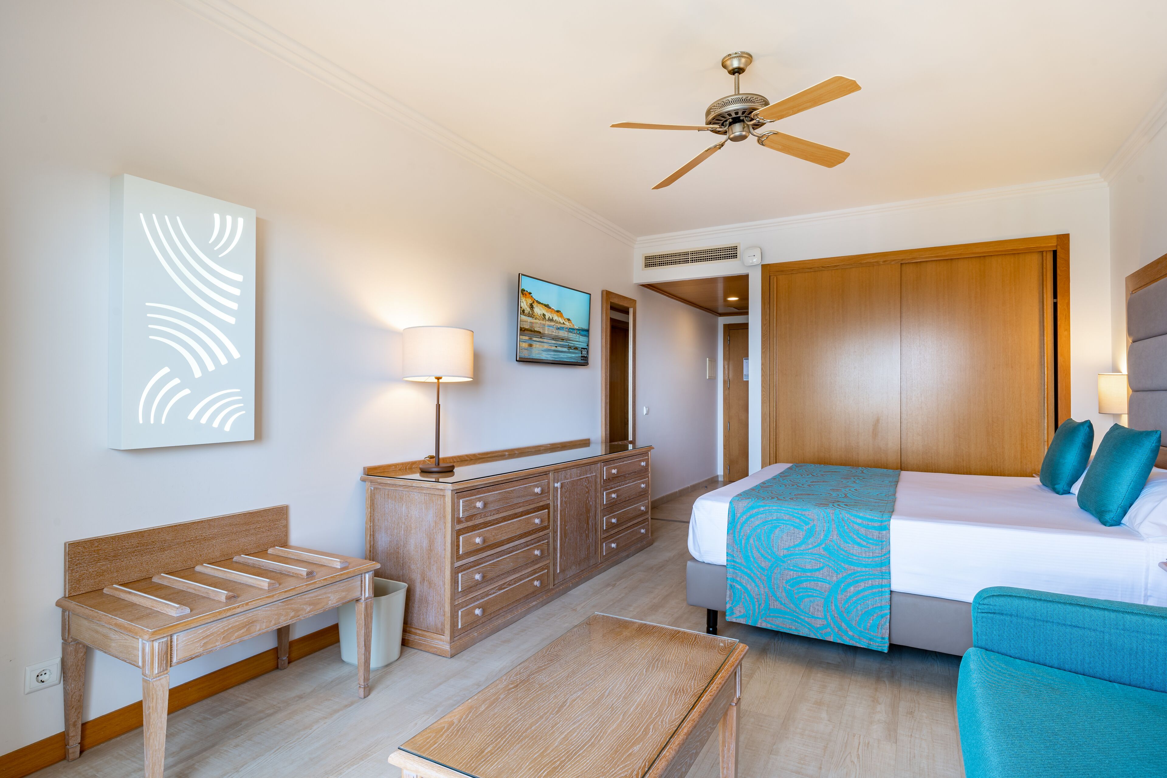 Una habitación de hotel con cama, escritorio, cómoda, ventilador de techo y un cuadro en la pared.