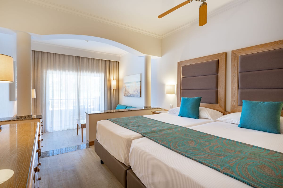 Habitació d'hotel amb dos llits, una taula de treball i una finestra gran amb cortines.