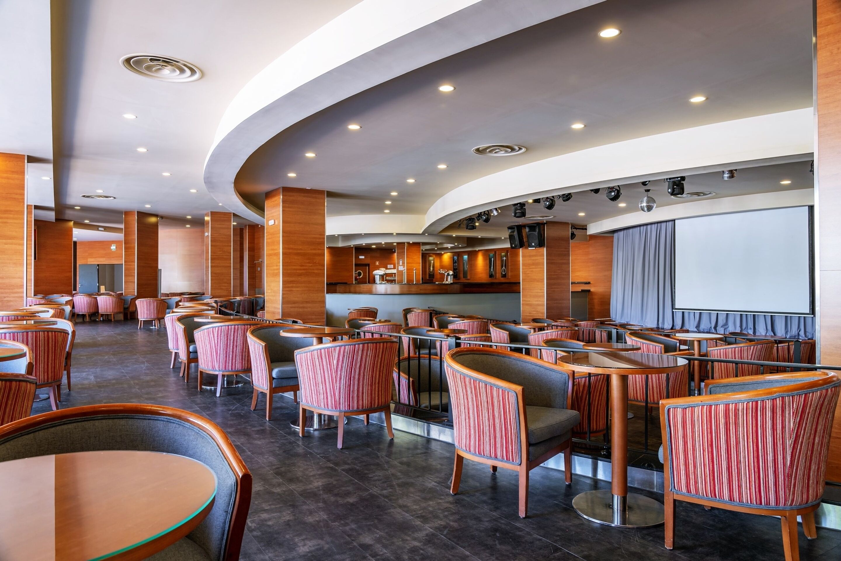 Un restaurante moderno con techo curvo, iluminación empotrada y sillas tapizadas a rayas.