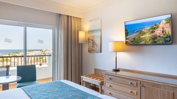 Habitación de hotel con cama, escritorio, silla, televisor y balcón con vista al mar.
