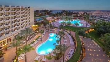 Un resort con una gran piscina, varias zonas de descanso y vista al océano.