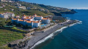A coastal hotel with multiple buildings, a beach, and a rocky shoreline. - Hotel Riu Madeira - All Inclusive (Santa Cruz)