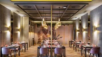 Un restaurante con varias mesas y sillas, un techo decorativo e iluminación en la pared.