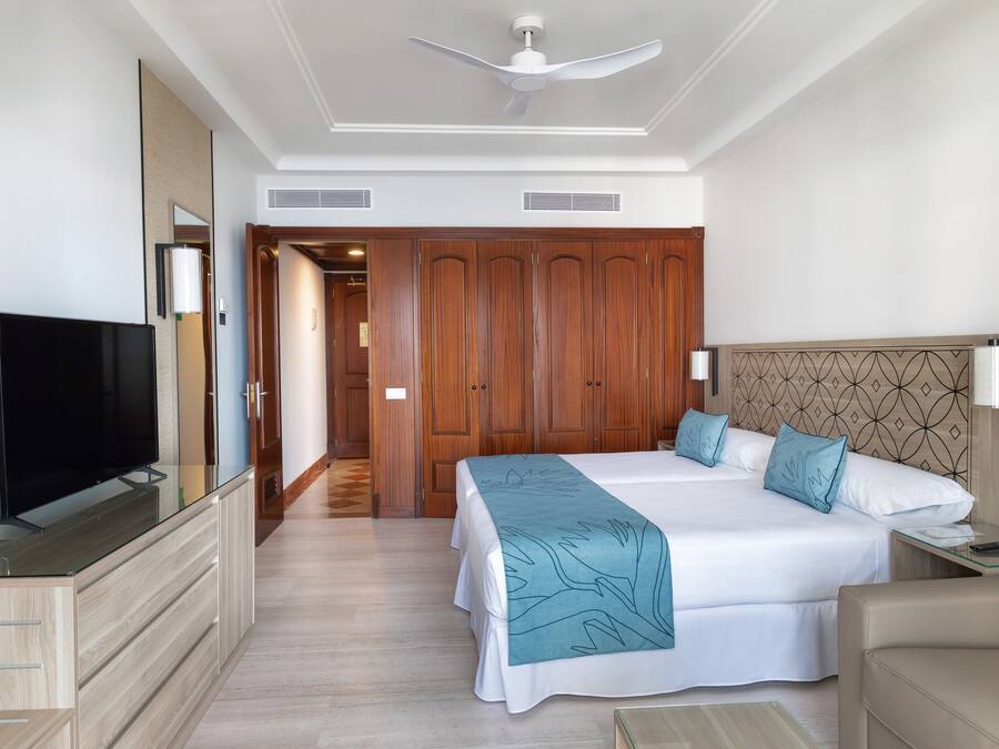 Ein Hotelzimmer mit einem großen Bett, einem Fernseher, einem Kleiderschrank und einem Deckenventilator.