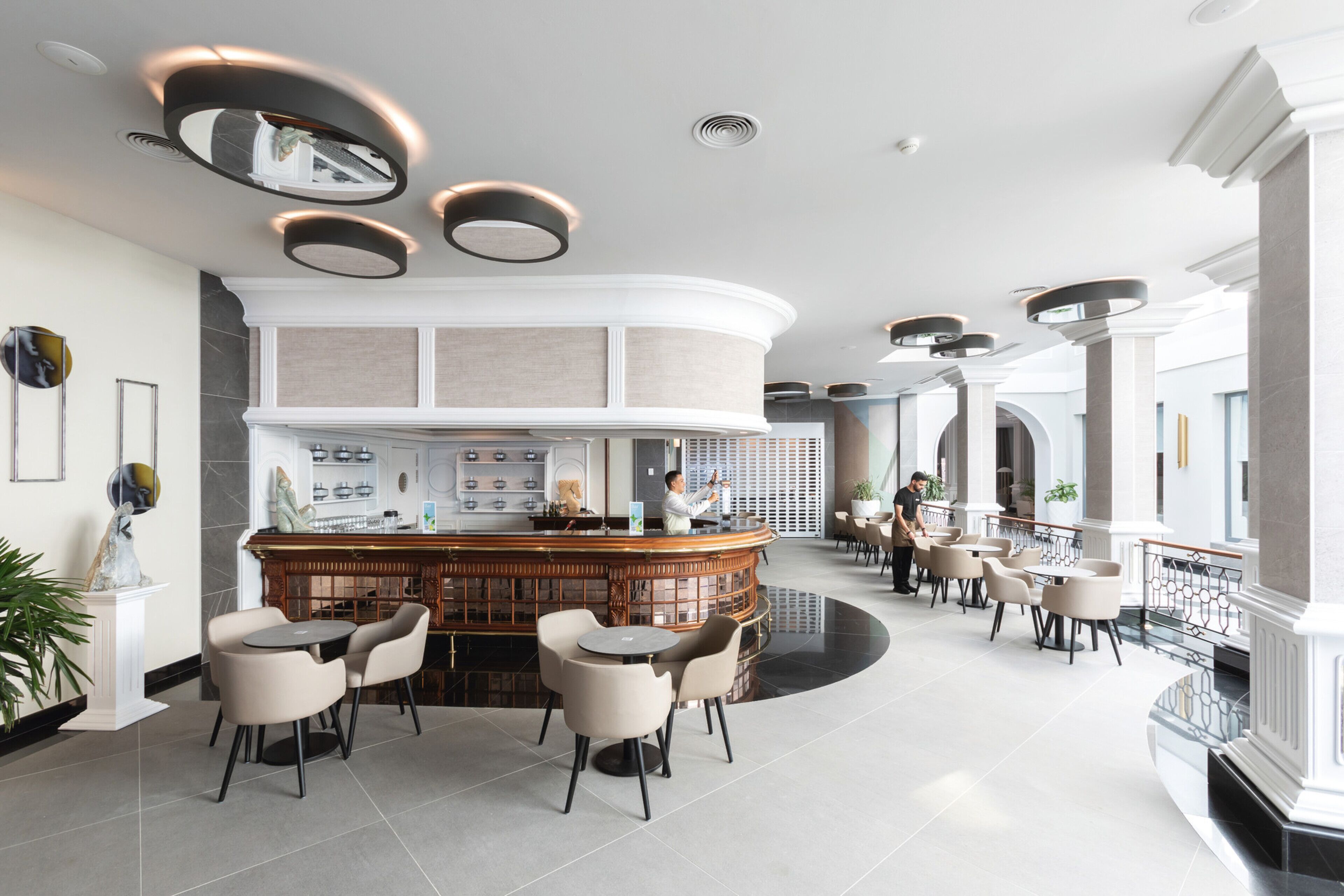 A modern hotel lobby with a central bar area, seating arrangements, and a spacious layout.