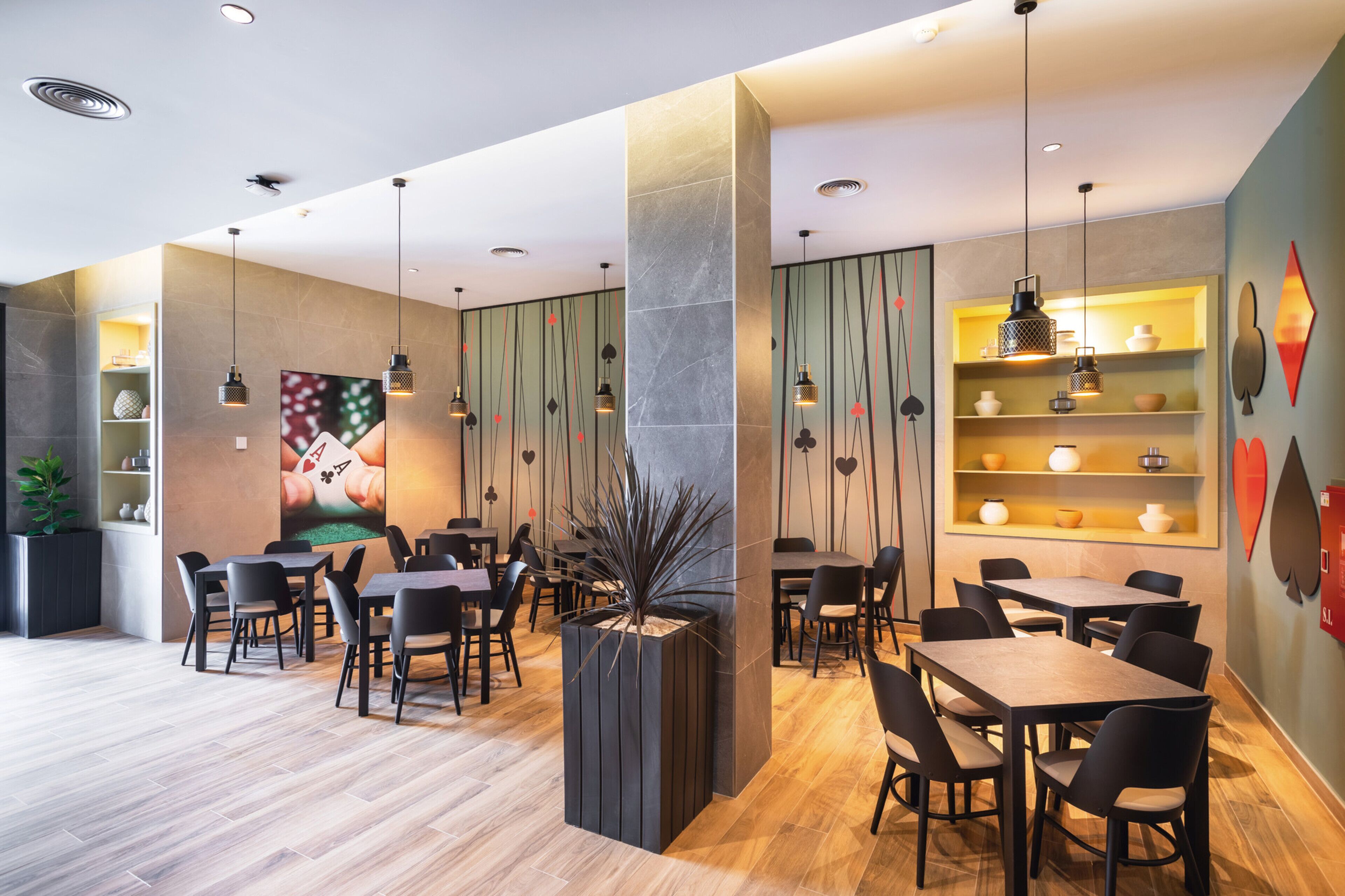 Un comedor moderno con mesas y sillas de madera, iluminación colgante y estantes decorativos.