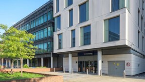 A modern building with a Travelodge sign, large windows, and a brick planter with greenery. - Travelodge London Ealing (London)
