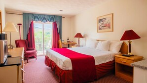 A hotel room with a large bed, a desk, a chair, a TV, and a balcony with curtains. - Country View Motor Inn (Kamloops)