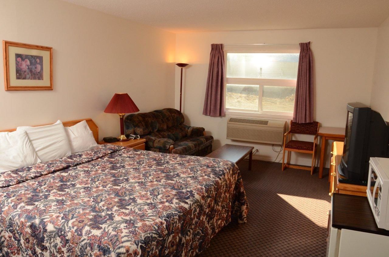 A hotel room with a large bed, a sofa, a TV, and a desk with a chair.