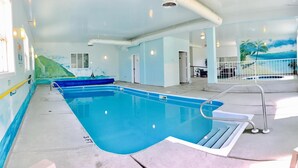 An indoor swimming pool with clear water, a diving board, and a mural of a beach scene on the wall.
