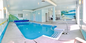 An indoor swimming pool with clear water, a diving board, and a mural of a beach scene on the wall.