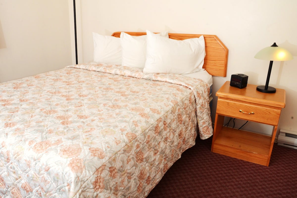 A neatly made bed with a floral bedspread, a wooden headboard, and a bedside table with a lamp and a radio.