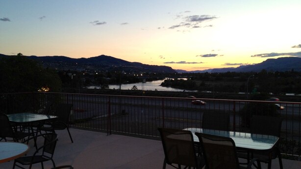 An outdoor patio with tables and chairs, overlooking a river and distant hills. - Country View Motor Inn (Kamloops)
