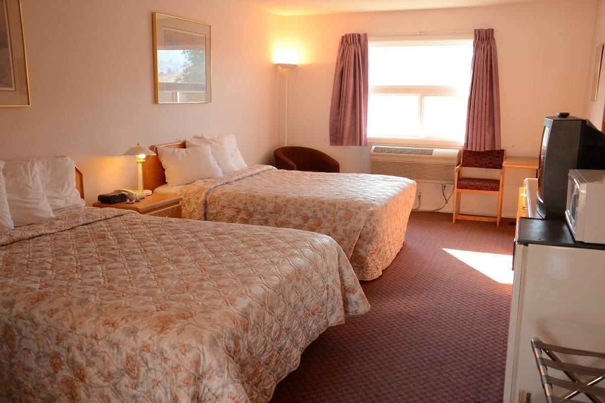 A hotel room with two beds, a desk, a chair, a television, and an air conditioning unit.