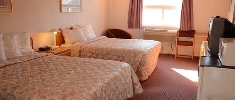 A hotel room with two beds, a desk, a chair, a television, and an air conditioning unit.