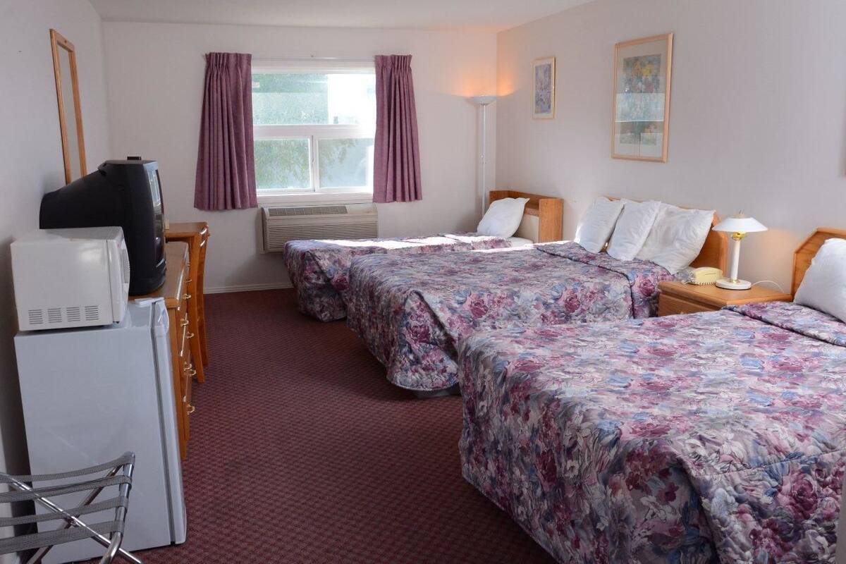 A hotel room with two beds, a desk with a television, a chair, and a small refrigerator.