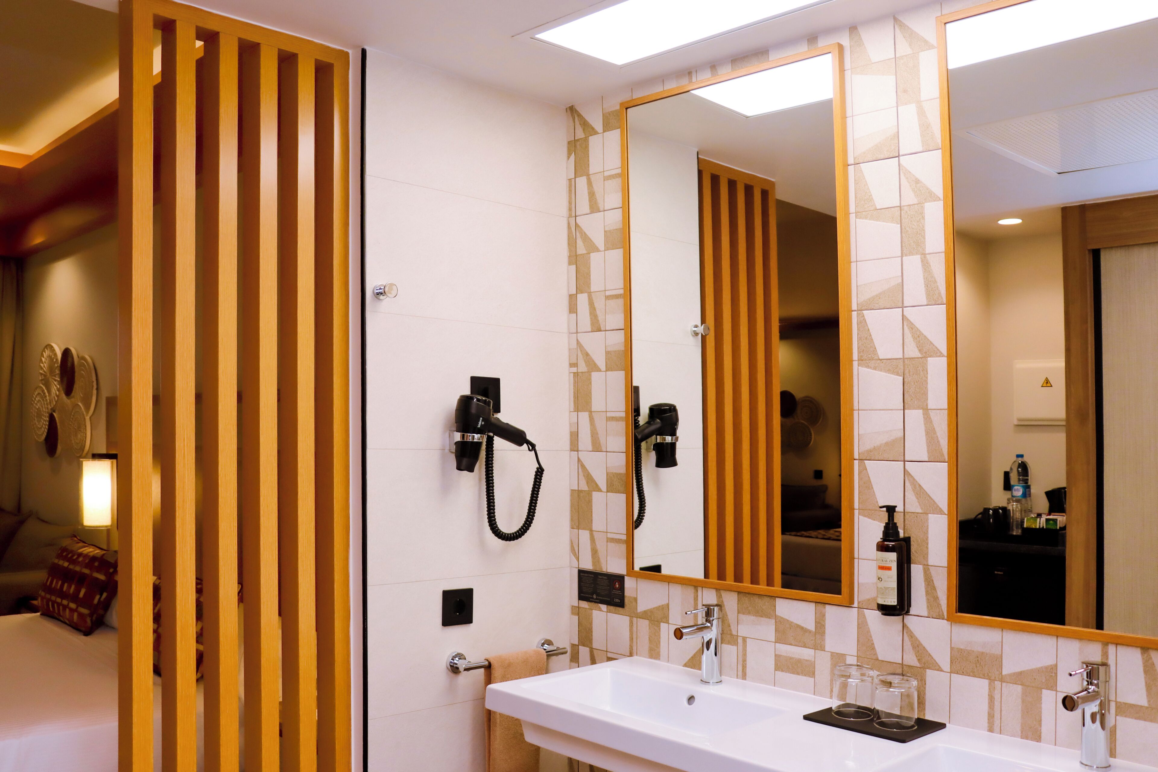 A hotel bathroom with a large mirror, a sink, a hairdryer, and a towel rack.