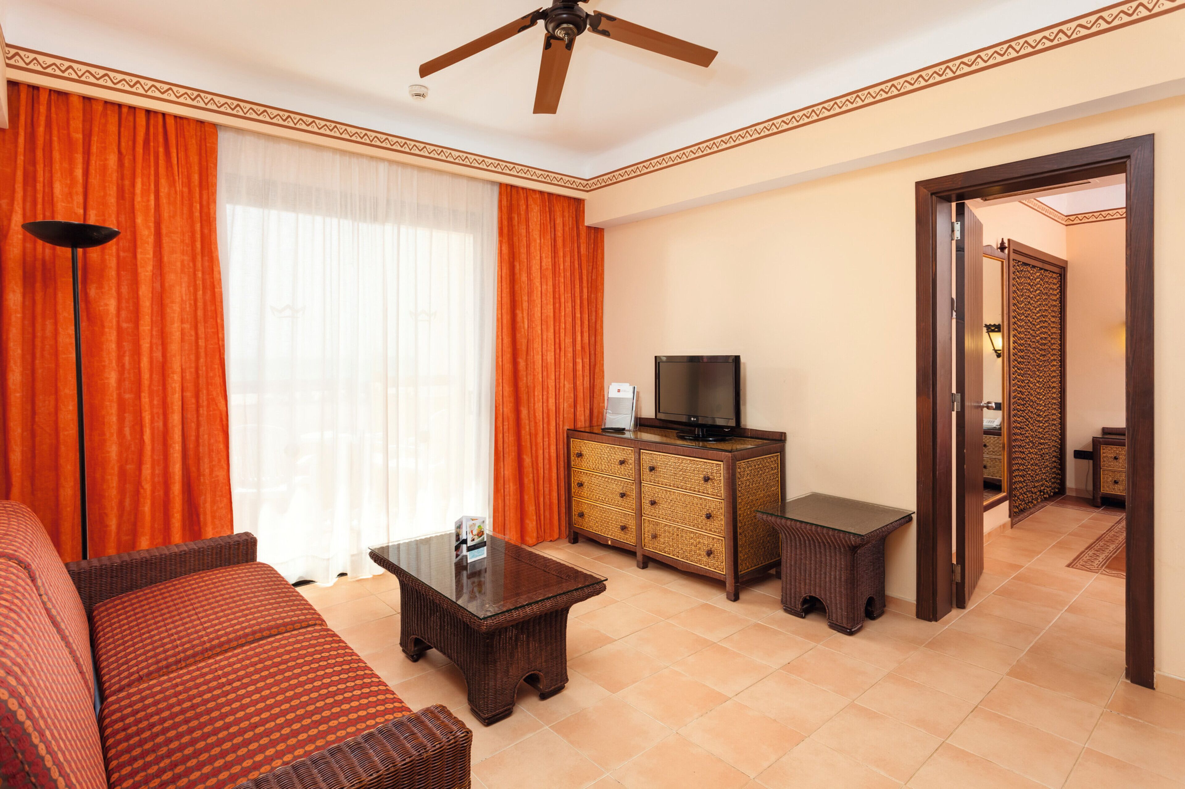 A living room with a sofa, a coffee table, a television on a cabinet, and a ceiling fan.