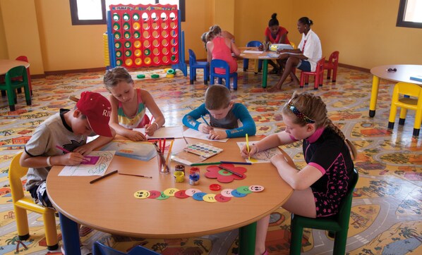 A group of children engaged in a craft activity at a round wooden table with colorful materials.
