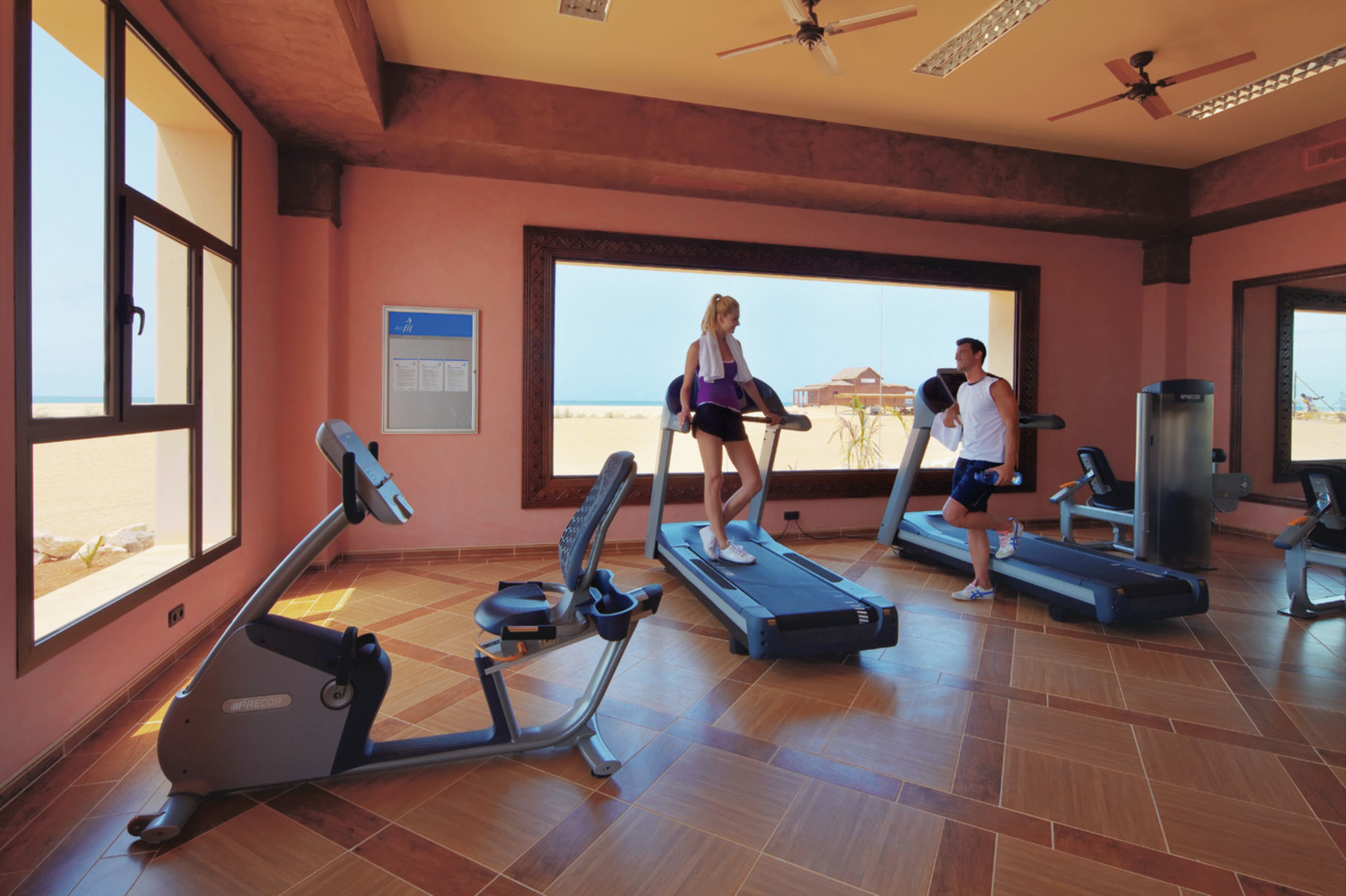 Un gimnasio con cintas de correr, bicicletas estáticas y un amplio ventanal con vistas a la playa.