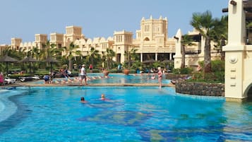 Relax by the pool surrounded by palm trees and resort buildings with arched windows.